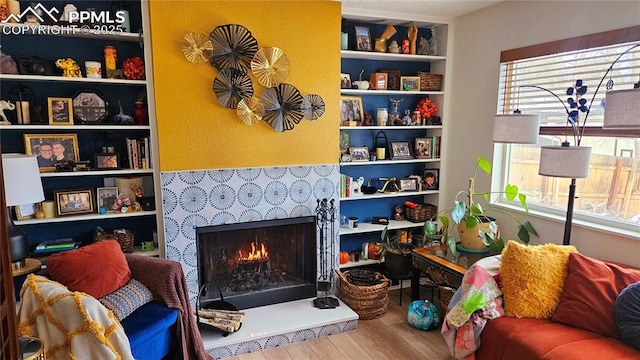 sitting room featuring hardwood / wood-style floors, built in shelves, a tile fireplace, and a healthy amount of sunlight