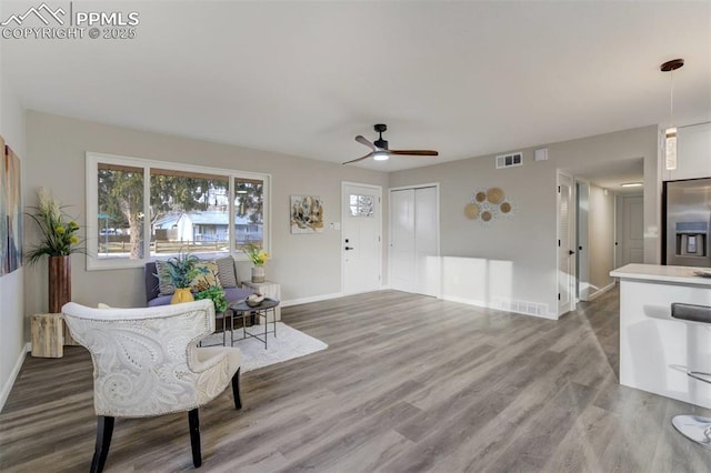 living area with a ceiling fan, wood finished floors, visible vents, and baseboards