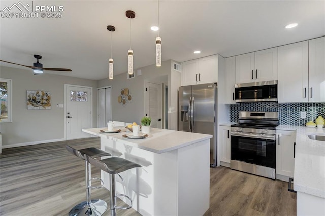 kitchen featuring light wood-type flooring, stainless steel appliances, a kitchen island, and backsplash