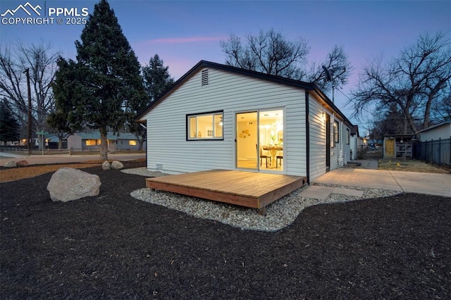 back of house at dusk featuring a deck and fence