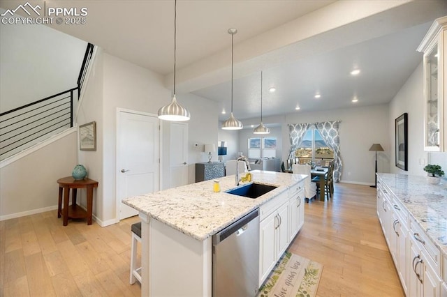 kitchen with an island with sink, sink, white cabinets, stainless steel dishwasher, and light hardwood / wood-style flooring