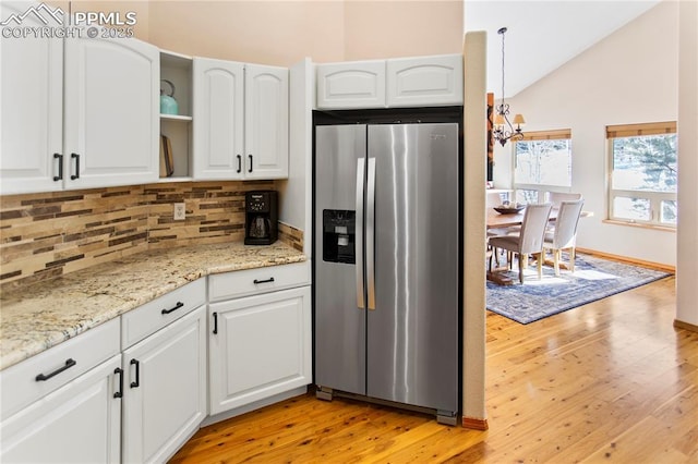 kitchen with tasteful backsplash, lofted ceiling, white cabinets, stainless steel refrigerator with ice dispenser, and light stone countertops