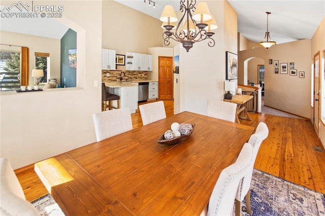 dining room with sink, a notable chandelier, light hardwood / wood-style floors, and high vaulted ceiling