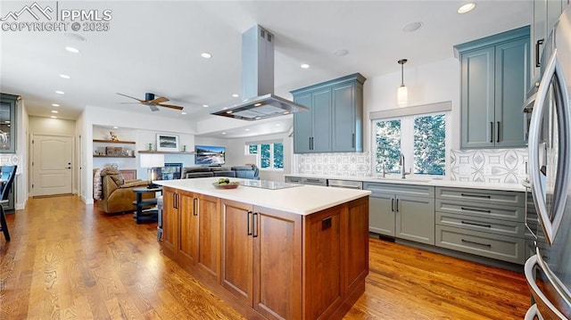 kitchen featuring island range hood, stainless steel refrigerator, sink, hanging light fixtures, and light hardwood / wood-style flooring