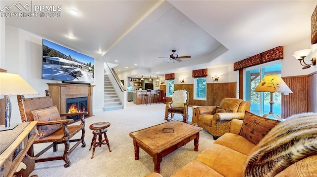 living room featuring light carpet, ceiling fan, and wood walls