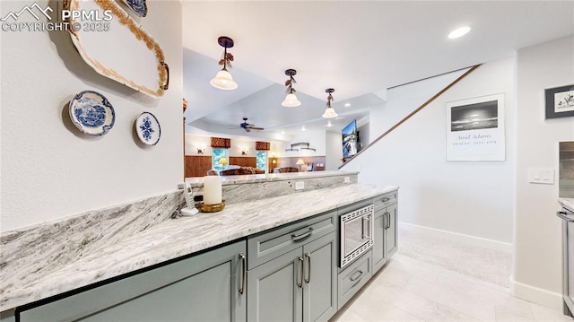 kitchen featuring pendant lighting, stainless steel microwave, gray cabinetry, ceiling fan, and light stone countertops