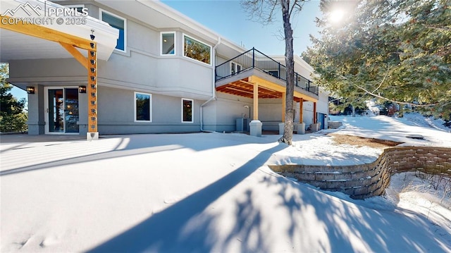 snow covered rear of property featuring central AC unit