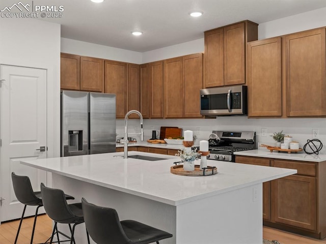 kitchen with appliances with stainless steel finishes, an island with sink, sink, a kitchen breakfast bar, and light wood-type flooring