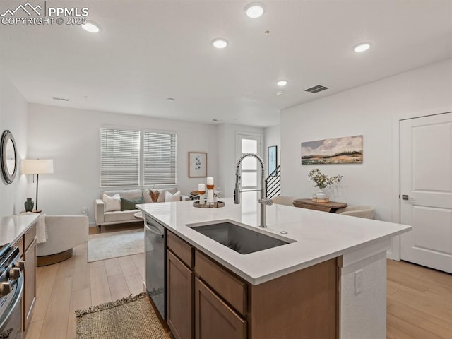 kitchen with stainless steel appliances, sink, a center island with sink, and light hardwood / wood-style floors