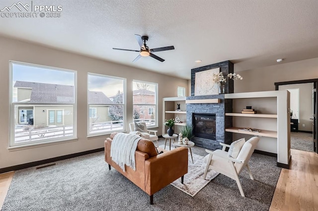 living room with ceiling fan, a textured ceiling, a fireplace, and light hardwood / wood-style flooring