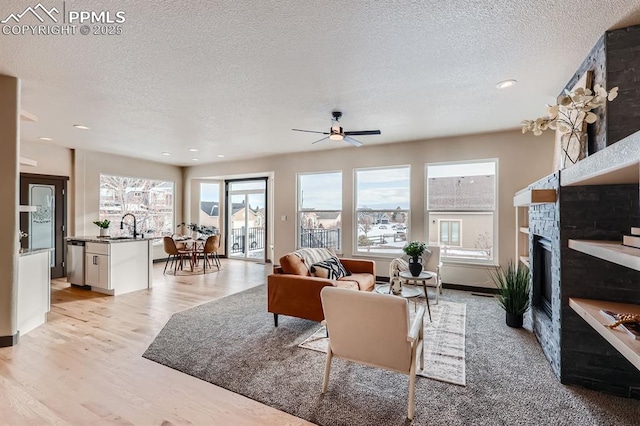 living room featuring sink, light hardwood / wood-style flooring, a textured ceiling, and ceiling fan