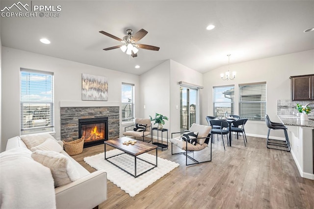 living room featuring lofted ceiling, ceiling fan with notable chandelier, a fireplace, and light hardwood / wood-style flooring