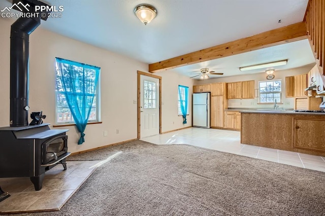 carpeted living room featuring sink, ceiling fan, beamed ceiling, and a wood stove