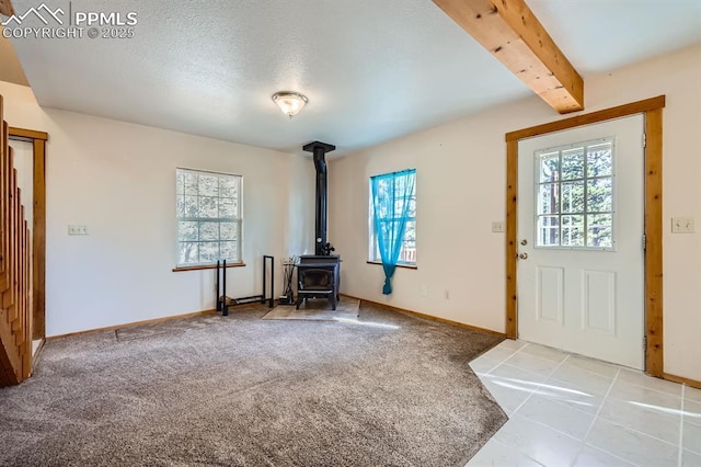 foyer with beamed ceiling, a textured ceiling, carpet, and a wood stove