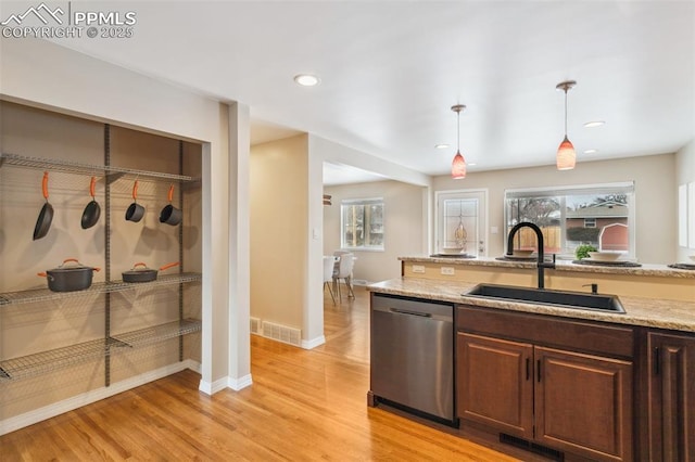 kitchen featuring decorative light fixtures, sink, stainless steel dishwasher, light stone counters, and light wood-type flooring