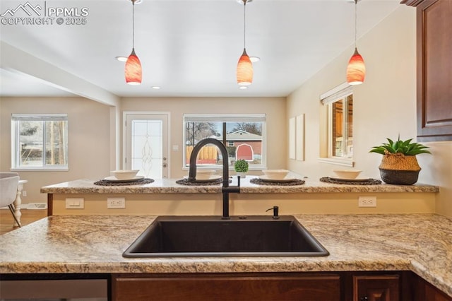 kitchen with sink, decorative light fixtures, a wealth of natural light, and light stone countertops