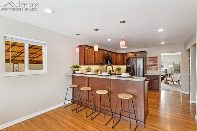 kitchen featuring pendant lighting, stainless steel appliances, kitchen peninsula, and light wood-type flooring