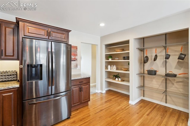 kitchen featuring light stone counters, built in shelves, light wood-type flooring, and stainless steel refrigerator with ice dispenser