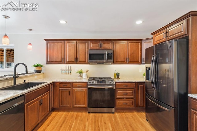 kitchen with sink, light stone counters, light wood-type flooring, pendant lighting, and stainless steel appliances