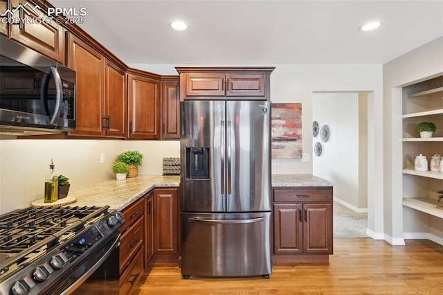 kitchen with light stone counters, appliances with stainless steel finishes, light hardwood / wood-style floors, and built in features