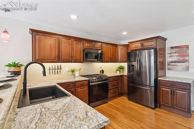 kitchen with stainless steel appliances, decorative light fixtures, light stone countertops, and sink