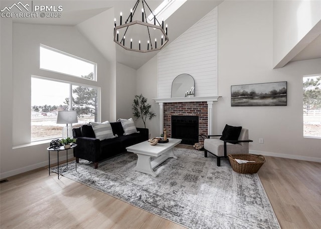 living room featuring high vaulted ceiling, light hardwood / wood-style floors, a chandelier, and a brick fireplace