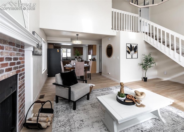 living room with a high ceiling, a brick fireplace, and light hardwood / wood-style floors