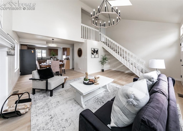 living room featuring a skylight, a chandelier, high vaulted ceiling, and light hardwood / wood-style flooring