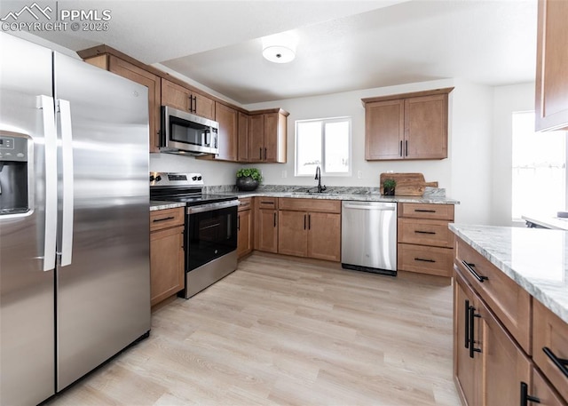 kitchen featuring light stone counters, sink, stainless steel appliances, and light wood-type flooring