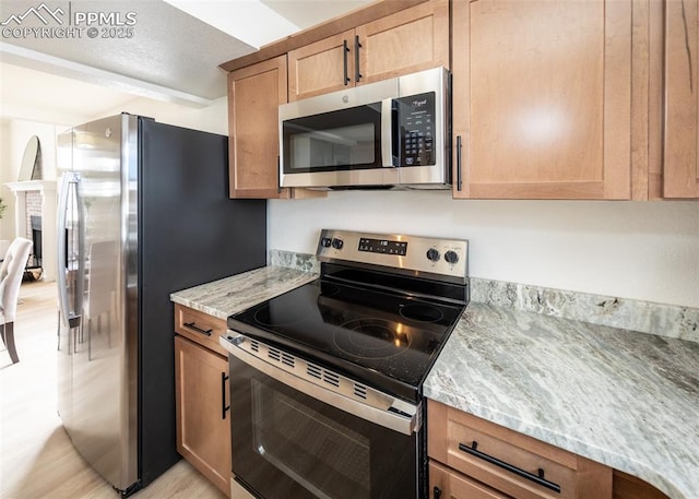 kitchen with stainless steel appliances, light stone counters, and light hardwood / wood-style floors