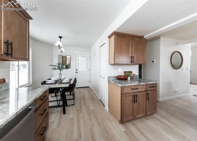 kitchen featuring light stone countertops, pendant lighting, stainless steel dishwasher, and light hardwood / wood-style flooring