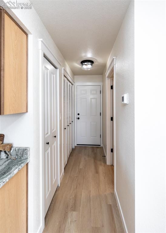 corridor with a textured ceiling and light hardwood / wood-style floors