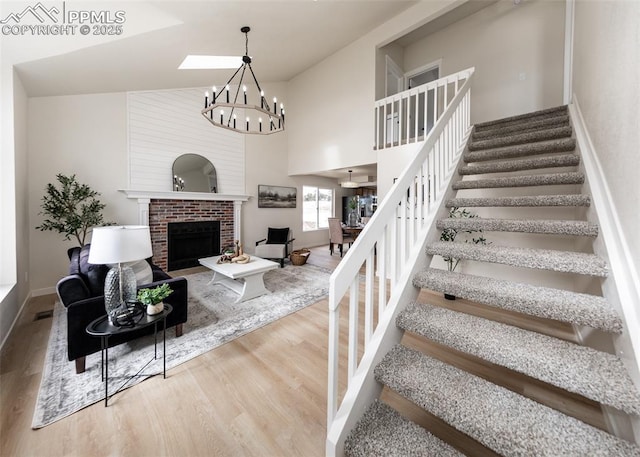 staircase featuring wood-type flooring, a towering ceiling, a notable chandelier, and a fireplace