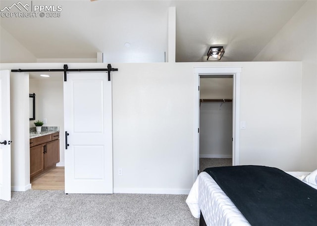 bedroom featuring light carpet, a spacious closet, a barn door, and ensuite bathroom