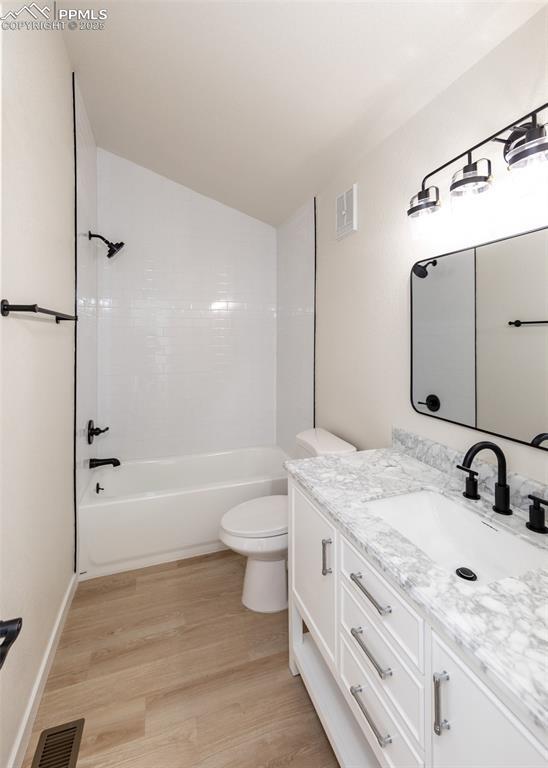 full bathroom featuring washtub / shower combination, toilet, wood-type flooring, vaulted ceiling, and vanity