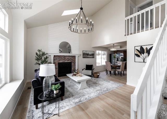 living room with an inviting chandelier, a brick fireplace, hardwood / wood-style floors, and high vaulted ceiling