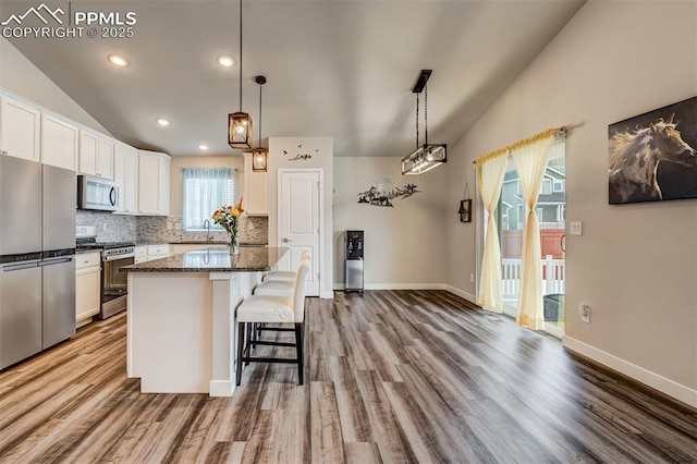 kitchen featuring lofted ceiling, stainless steel appliances, hanging light fixtures, and a kitchen island