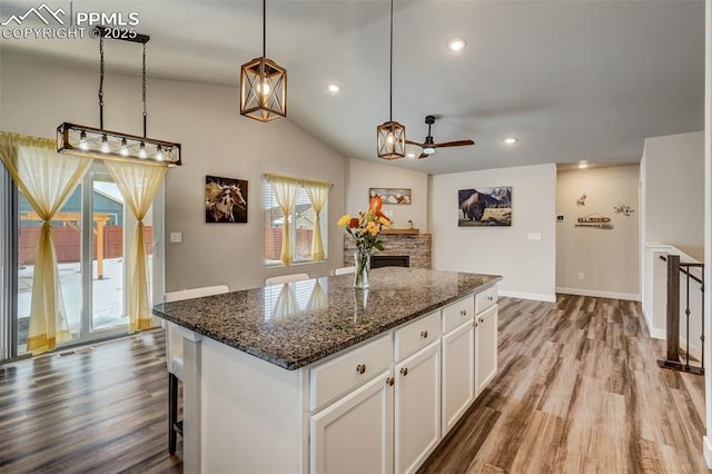 kitchen featuring pendant lighting, white cabinetry, a center island, a stone fireplace, and dark stone counters