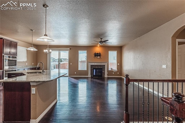 kitchen featuring dark hardwood / wood-style floors, sink, hanging light fixtures, ceiling fan, and light stone countertops