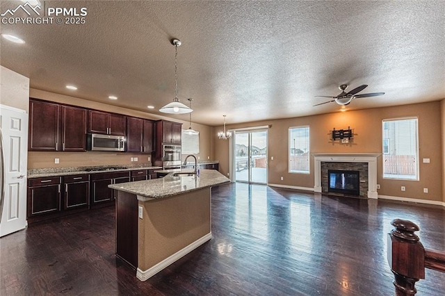 kitchen featuring sink, dark brown cabinets, light stone counters, an island with sink, and decorative light fixtures