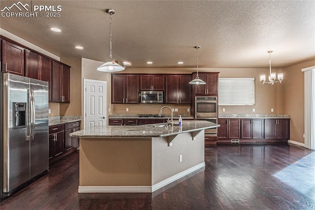 kitchen with decorative light fixtures, sink, dark hardwood / wood-style flooring, stainless steel appliances, and a center island with sink