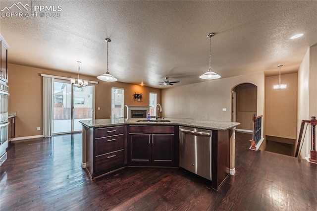 kitchen with sink, appliances with stainless steel finishes, hanging light fixtures, dark brown cabinetry, and light stone countertops