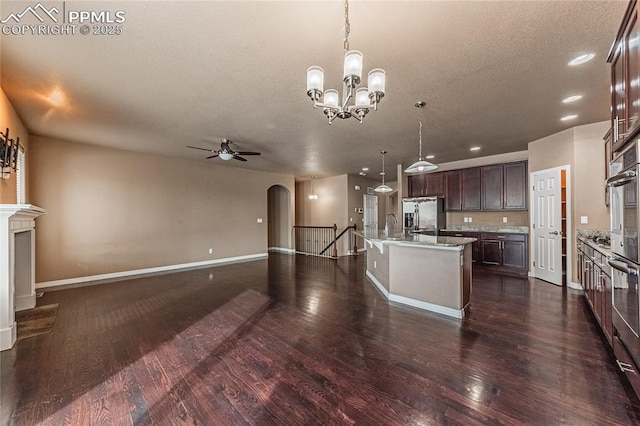 kitchen with appliances with stainless steel finishes, pendant lighting, an island with sink, dark hardwood / wood-style flooring, and dark brown cabinets