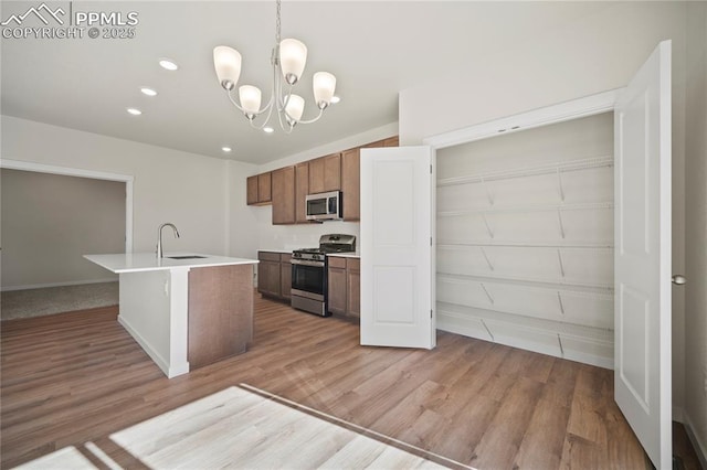 kitchen with pendant lighting, sink, light hardwood / wood-style flooring, stainless steel appliances, and a center island with sink