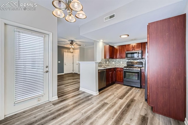 kitchen with stainless steel appliances, ceiling fan with notable chandelier, backsplash, and light wood-type flooring