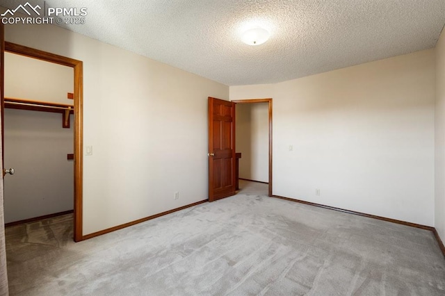 unfurnished bedroom with a textured ceiling, light colored carpet, baseboards, a closet, and a walk in closet