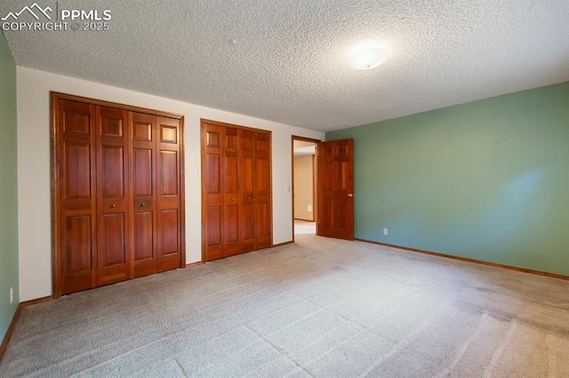 unfurnished bedroom with baseboards, a textured ceiling, two closets, and light colored carpet