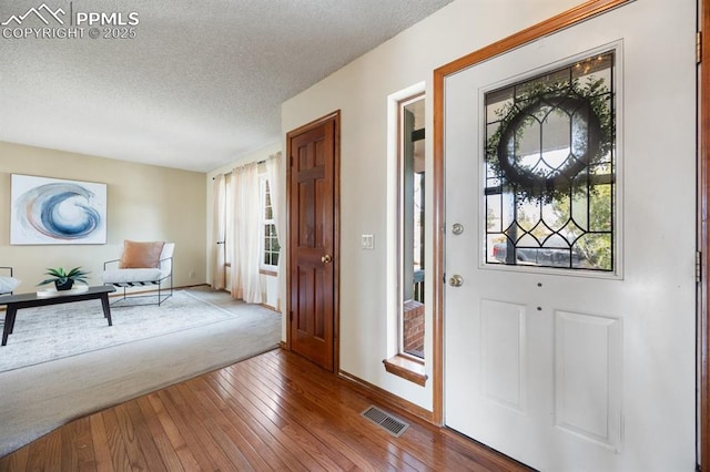 foyer featuring a textured ceiling, hardwood / wood-style flooring, visible vents, and baseboards