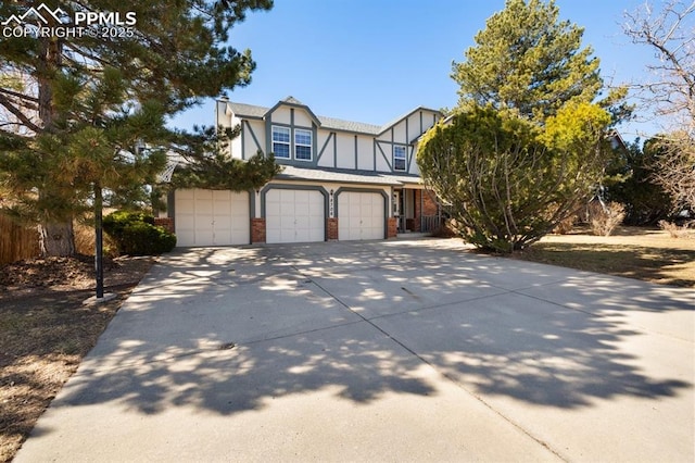 tudor-style house featuring a garage, driveway, brick siding, and stucco siding