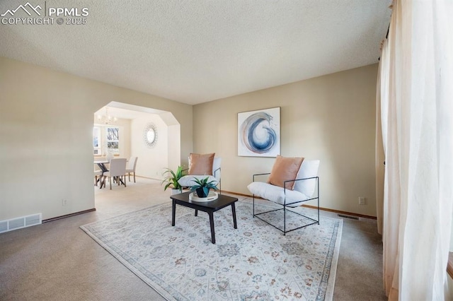 sitting room featuring visible vents, arched walkways, baseboards, carpet, and a textured ceiling